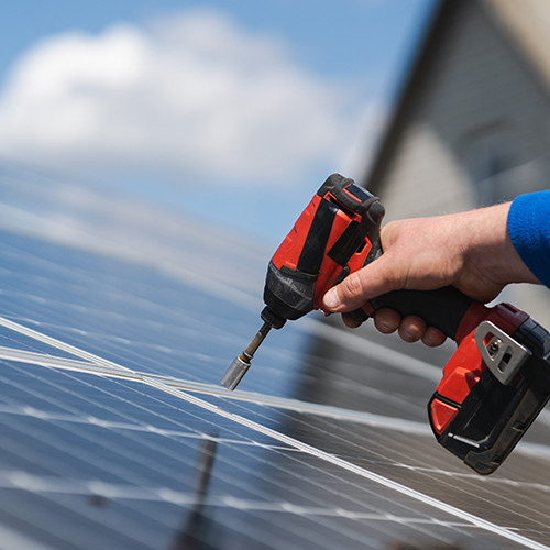 Electricians hand with a drill screwdriver, fitting or repairing solar panels on a roof