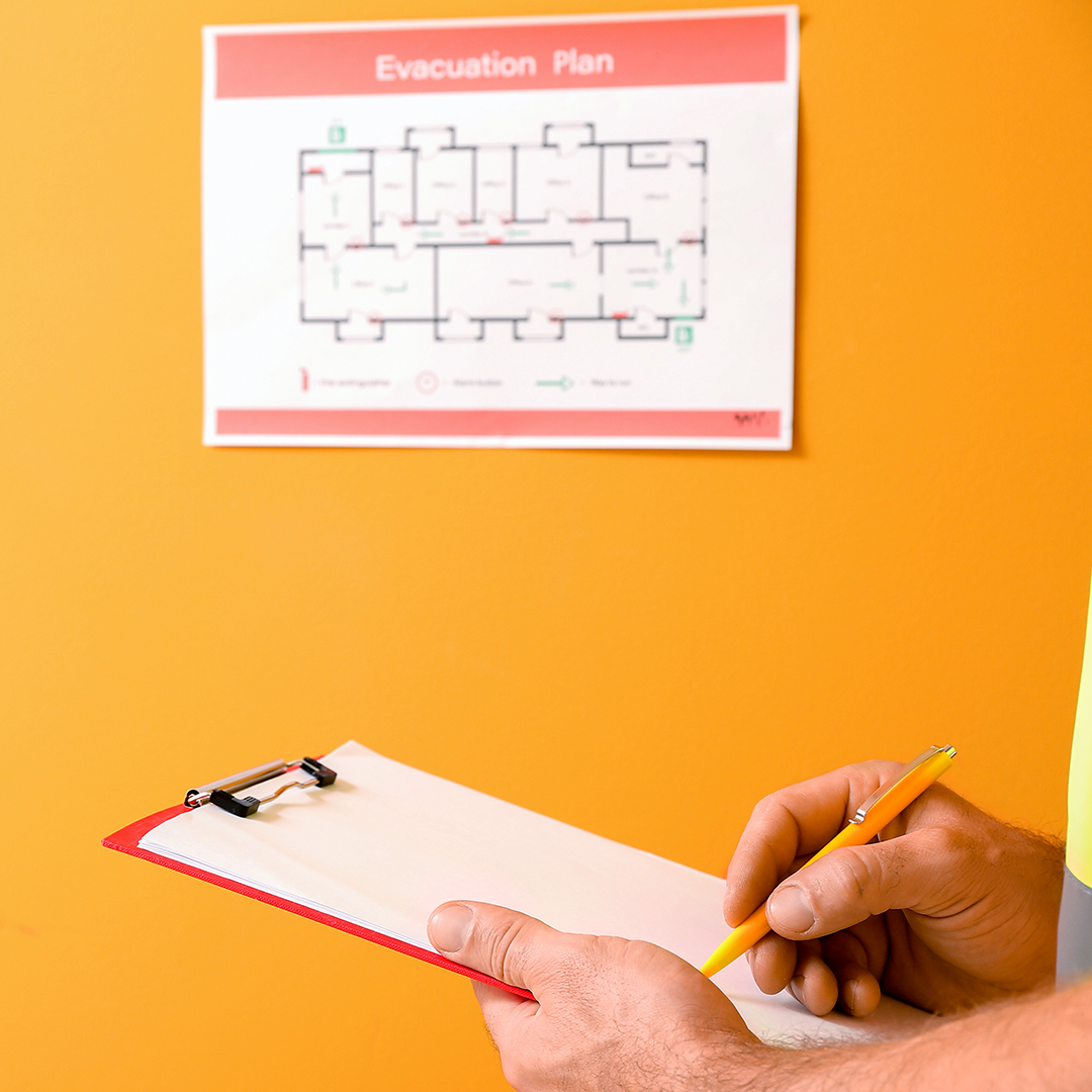 Person with a clipboard standing next to an Evacuation plan on the wall